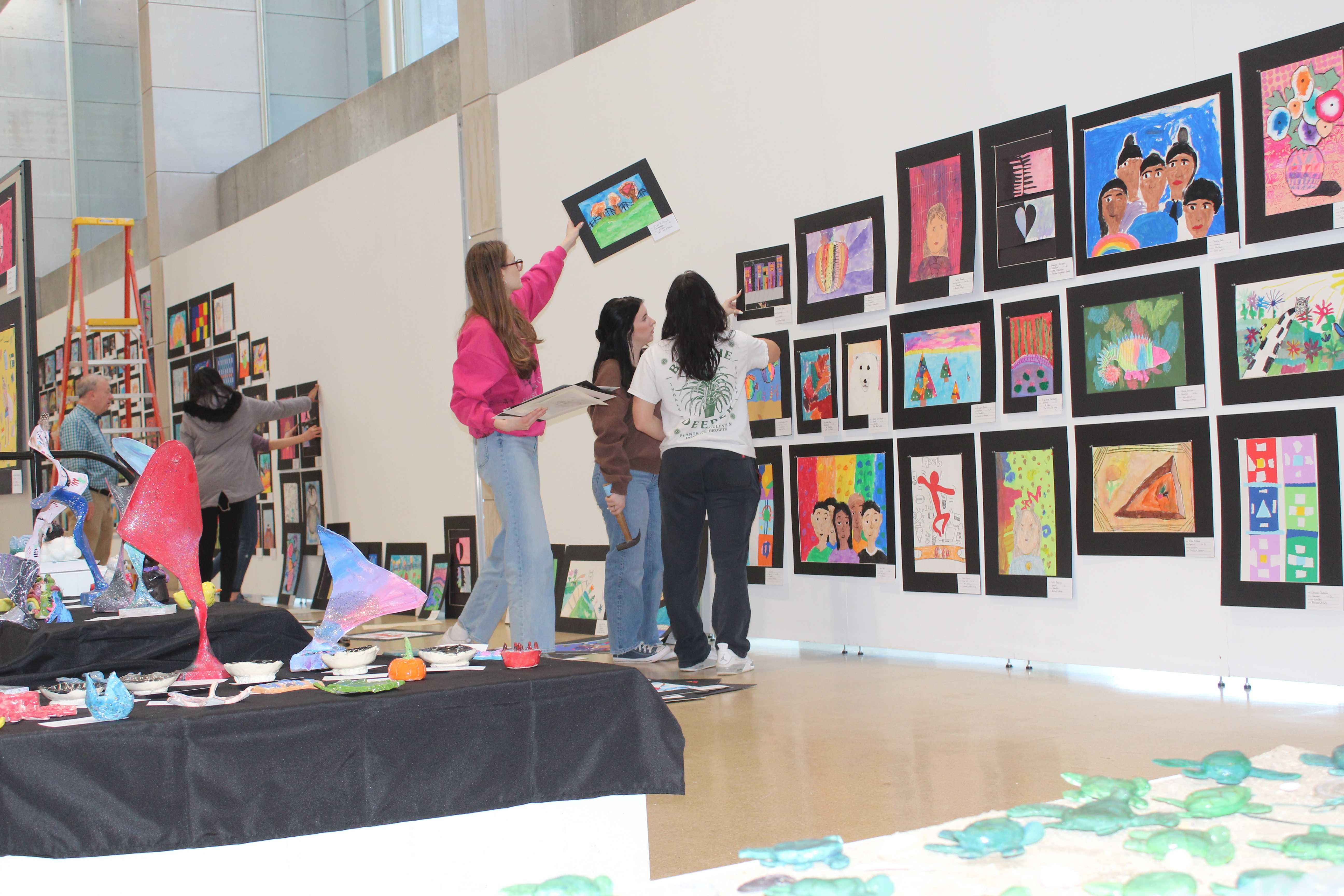 Students are putting up pieces of artwork at the gallery for the upcoming art show